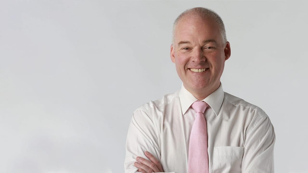 Smiling bald man wearing a white dress shirt and pink tie with arms crossed.