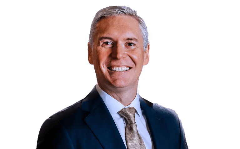 Smiling middle-aged man with graying hair wearing a dark suit and a gold tie.