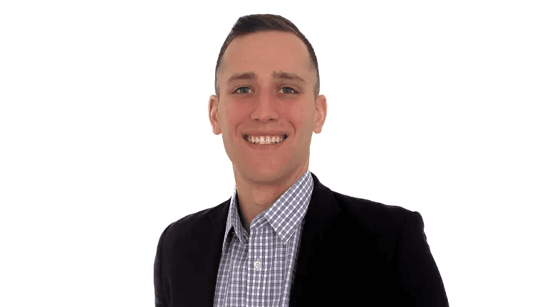 Smiling young man in a blue checkered shirt and black blazer against white background.