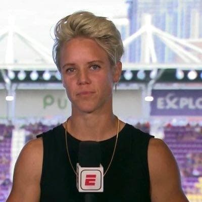 Short-haired blonde woman wearing a black top and gold chain holding an ESPN microphone.